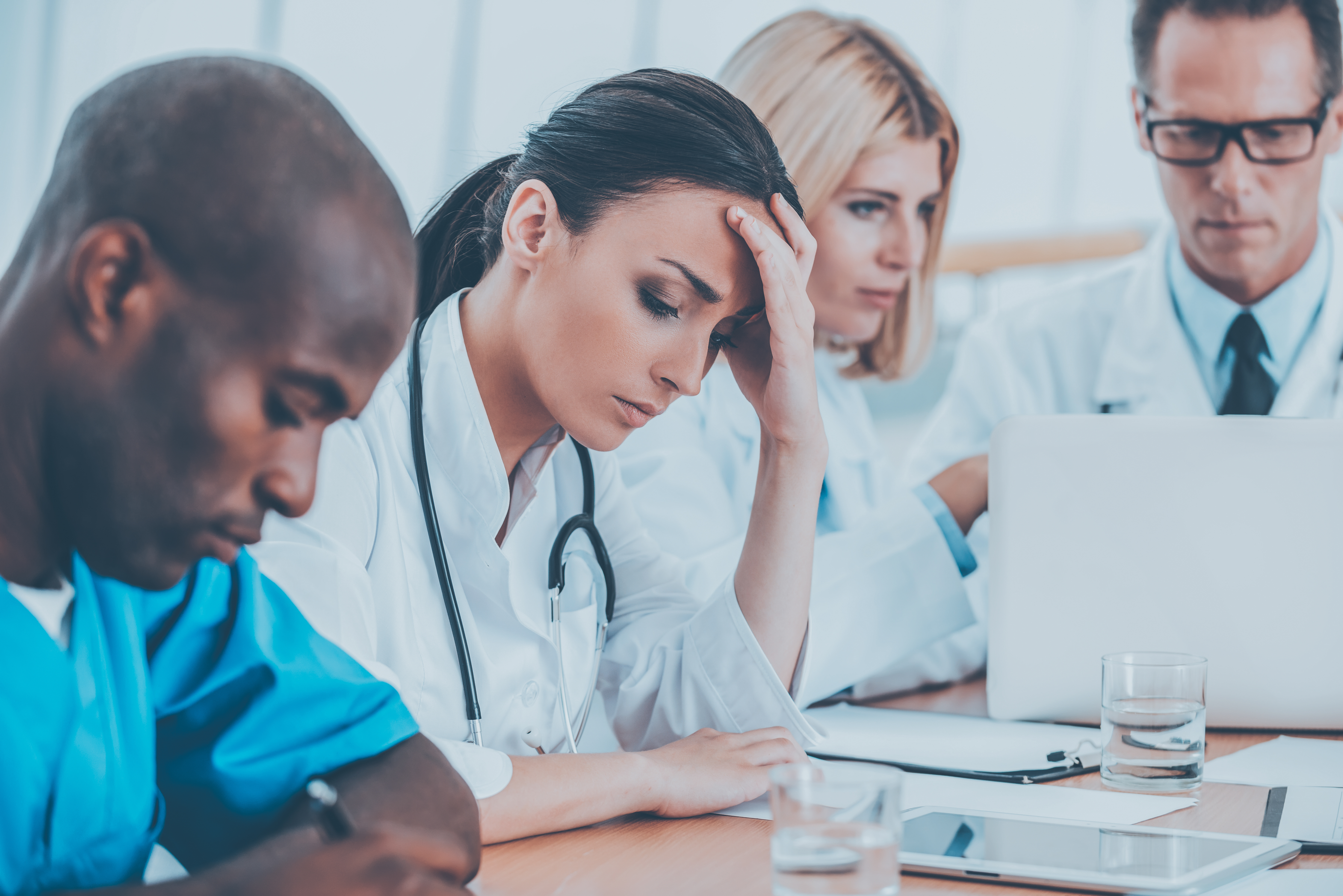 Feeling so tired. Depressed young female doctor holding hand in hair while sitting together with her colleagues at the meeting