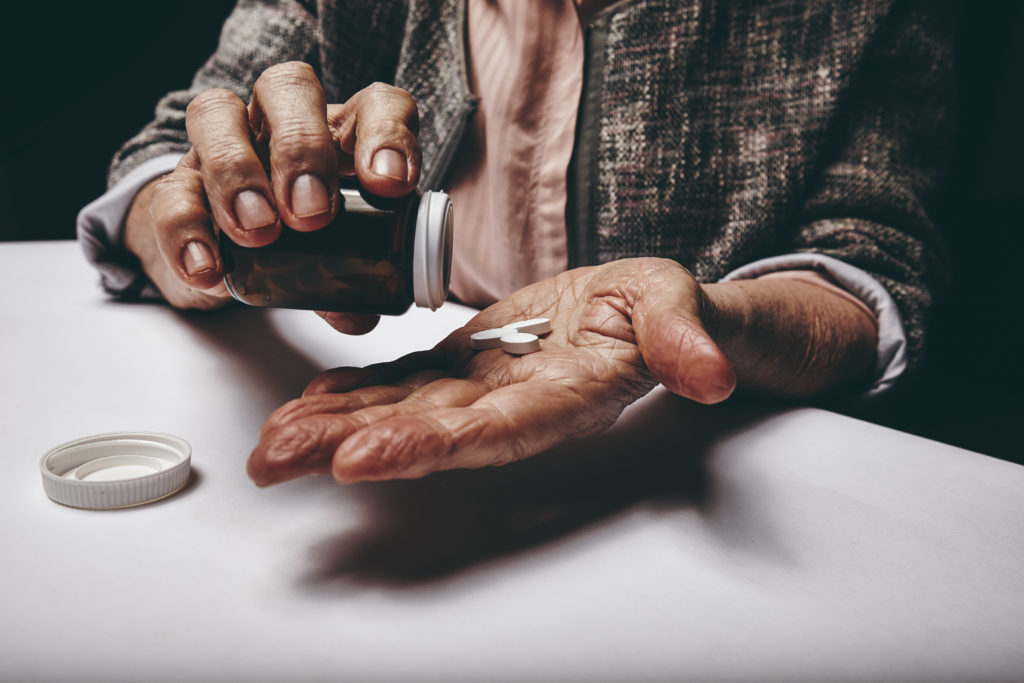 Woman sitting at a table shaking a pill out of a pill bottle.